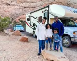 Family of four posing happily in front of their RV outdoors.