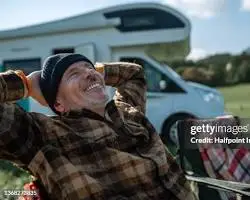 Man relaxing outdoors with a van in the background.